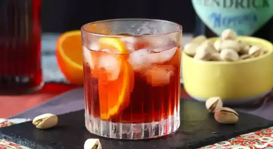 Przepis na Negroni Sbagliato: orzeźwiający drink z pomarańczą i lodem, obok miseczka pistacji.