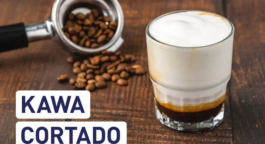 Kawa cortado z mleczną pianką, obok portafilter z ziarnami kawy. Idealny napój na poranek.