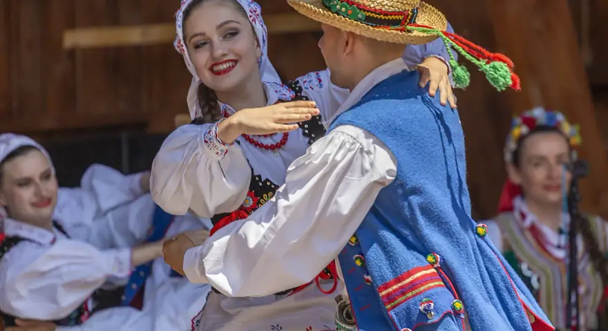 Uśmiechnięta para w tradycyjnych strojach tańczy do skocznych piosenek ludowych.