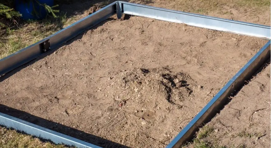Metalowa rama na ziemi, gotowa na zrobienie fundamentu pod szklarnię.