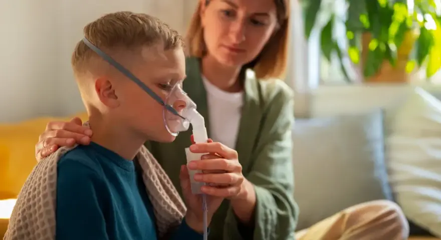 Chłopiec z maską nebulizatora, wspierany przez matkę. Dbałość o zdrowie dziecka z astmą wczesnodziecięcą.