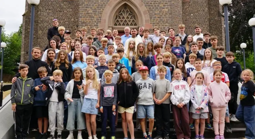 Große Gruppe von Kindern und Jugendlichen vor einer Kirche, die an einem christlichen Ferienlager teilnehmen.