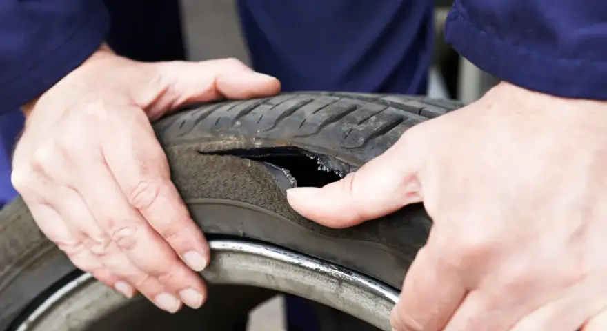 Dłonie mechanika badają oponę po głośnym wystrzale. Widoczne jest duże rozdarcie bieżnika.