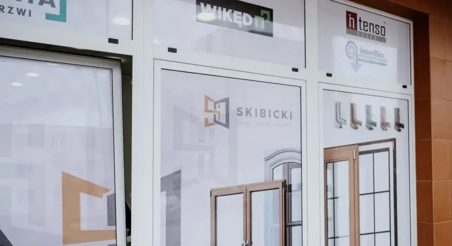 Witryna sklepowa z oknami i drzwiami, widoczne logotypy firm.