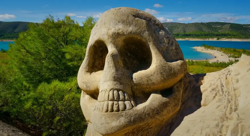 Escultura de calavera en la sacedon ruta de las caras, con un lago turquesa y montañas verdes al fondo.