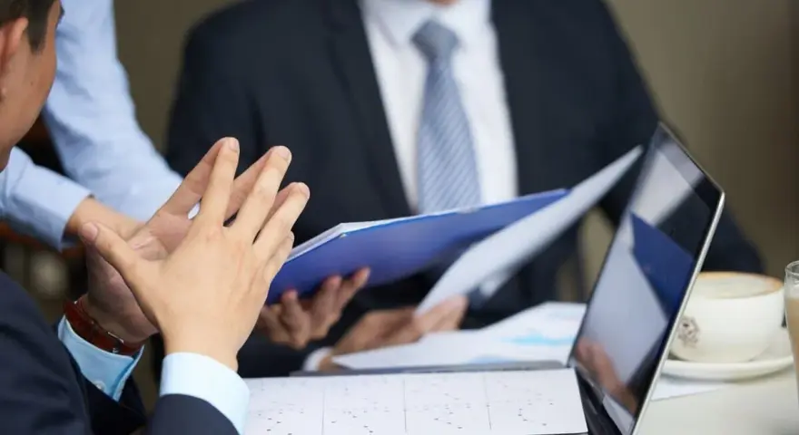 Personas discuten documentos y gráficos, quizás sobre la demora de calificación de incapacidad permanente.