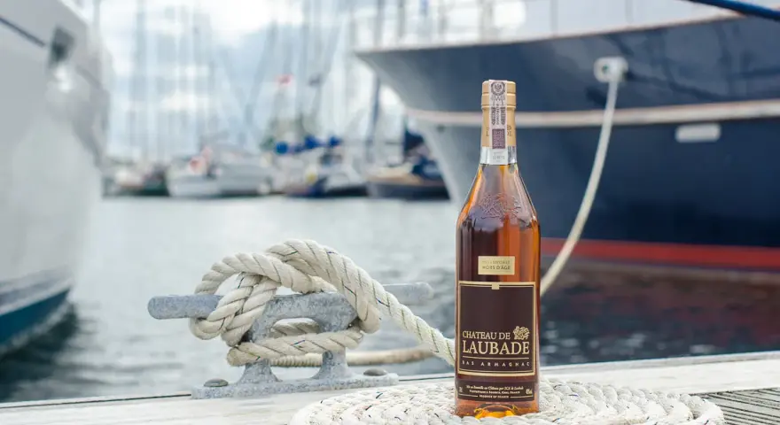 Butelka Bas Armagnac Chateau de Laubade stoi na tle jachtów. To doskonały trunek, jeśli zastanawiasz się, armaniak co to.