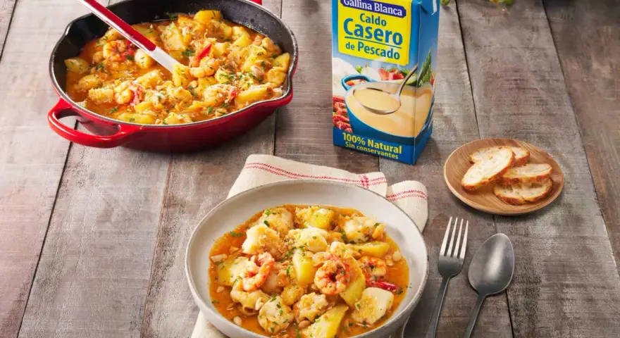 Un delicioso rape a la marinera, con patatas y gambas, servido en una cazuela roja y un plato.