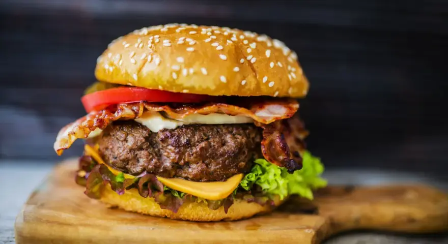 Hamburger di carne succulento con bacon croccante, formaggio fuso, pomodoro e lattuga su panino ai semi di sesamo.