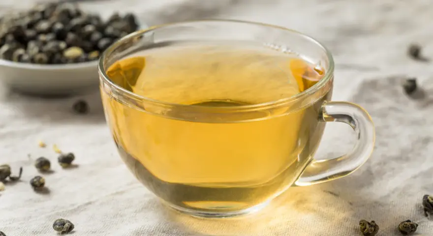 Zaparzona herbata oolong w szklance, obok miseczka z suszonymi liśćmi. Odkryj niezwykłe herbata oolong właściwości.