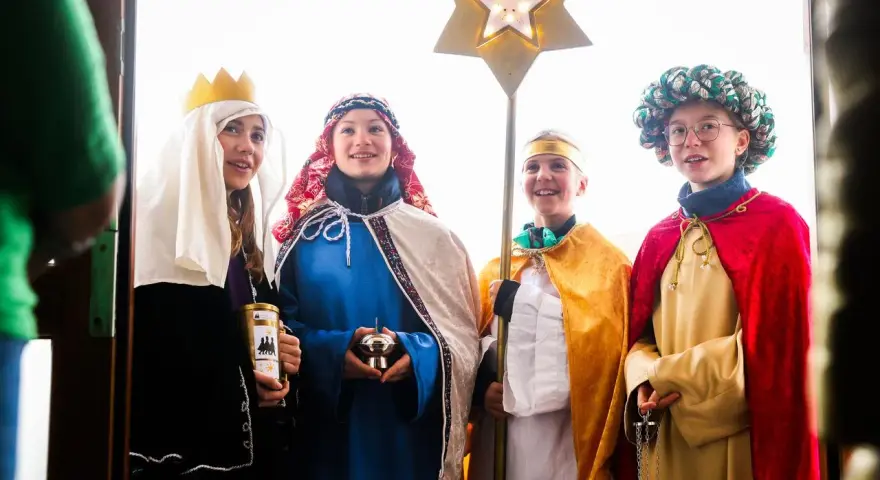 Vier Kinder als Sternsinger evangelisch verkleidet, mit Stern und Spendenbüchse, stehen vor einer Tür.