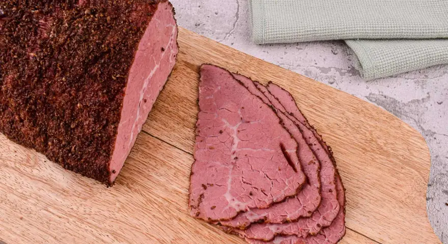 Kawałek pastrami, co to jest? Aromatyczne, peklowane i wędzone mięso wołowe, pokrojone w cienkie plastry, leży na desce.