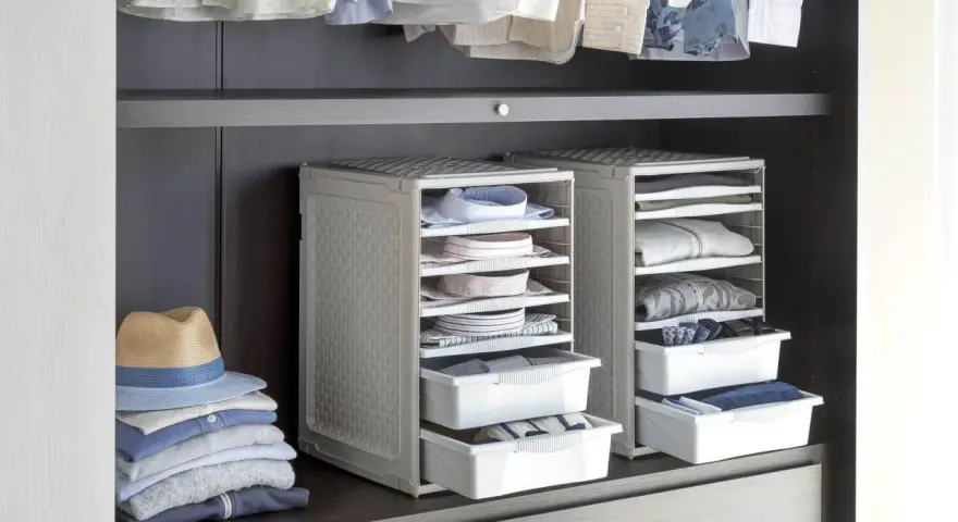 Organizzazione armadio: camicie piegate in contenitori modulari, pile di vestiti e un cappello su una mensola.