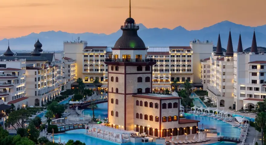 Luksusowy hotel z basenami i wieżą, idealny na wakacje all inclusive w Turcji. Góry w tle.