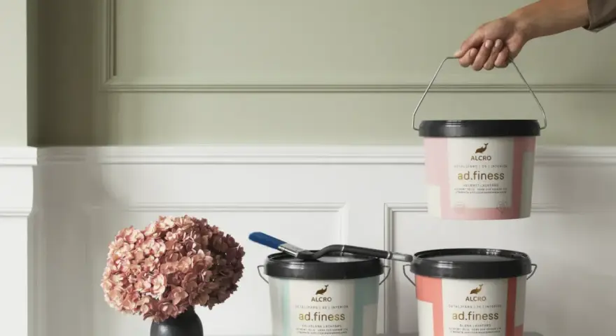 Tre burkar Alcro ad.finess färg i olika kulörer. En burk lyfts, en med pensel och en med en hortensia. Välj mellan sidenmatt vs matt för ditt projekt.