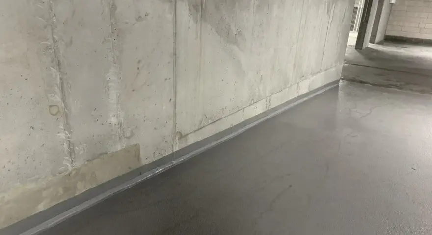 Szara, gładka posadzka w garażu, zabezpieczająca co na podłogę w garażu przed wilgocią. Betonowa ściana w tle.