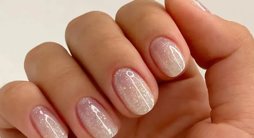 Nahaufnahme einer Hand mit ovalen Nägeln, die mit schimmerndem Glitzer-Nagellack in Pastelltönen verziert sind.