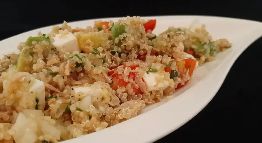 Salade colorée de quinoa avec des dés de feta, avocat, tomates et persil, servie dans un plat blanc.