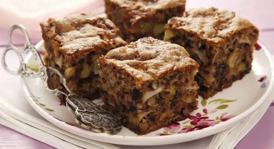 Vier Stücke saftiger Apfel Walnuss Kuchen auf einem Teller mit Blumenmuster, daneben ein antiker Tortenheber.