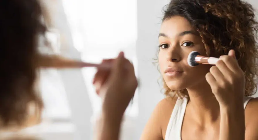 Une jeune femme applique du fond de teint avec un pinceau. Elle se demande combien de temps garder une palette de maquillage pour une peau parfaite.