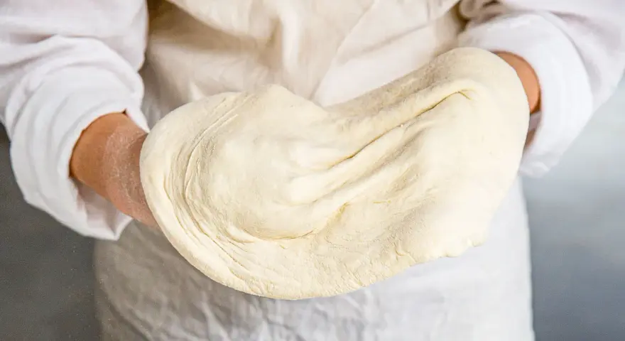 Hände halten geschmeidigen pizzateig, original rezept von einem italienischen gastronomen. Perfekt für authentische Pizza.