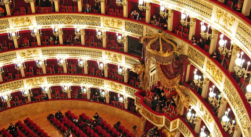 Elegancka loża w teatrze, z czerwonymi aksamitnymi siedzeniami i złotymi zdobieniami, czeka na widzów.