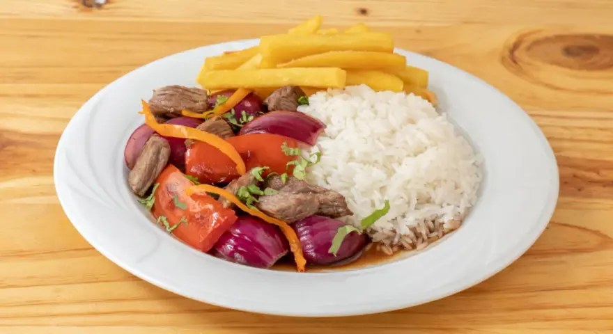 Lomo saltado con arroz blanco, papas fritas, carne, cebolla roja y tomate. Un plato peruano delicioso.