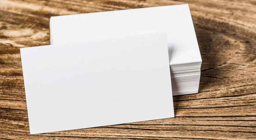 Pila de tarjetas de visita blancas sobre madera. Se aprecian los diferentes grosores de papel en la pila.