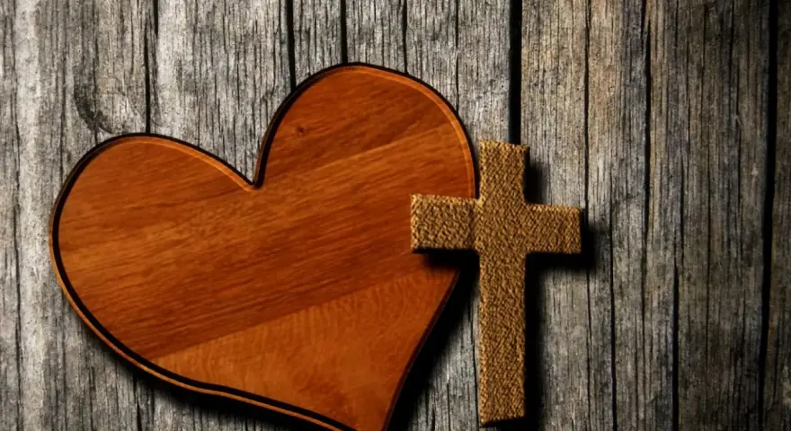 Holzherz und Kreuz auf grober Holzoberfläche. Ein Symbol für Liebe und Glauben, wie in Lukas 23,34.