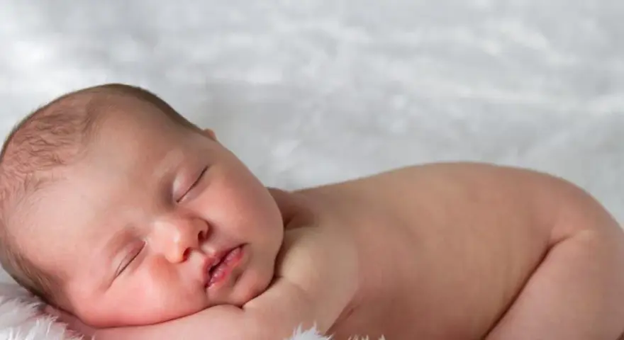 Śpiące, 3 miesięczne dziecko z delikatnymi włoskami, wtulone w miękkie futerko.