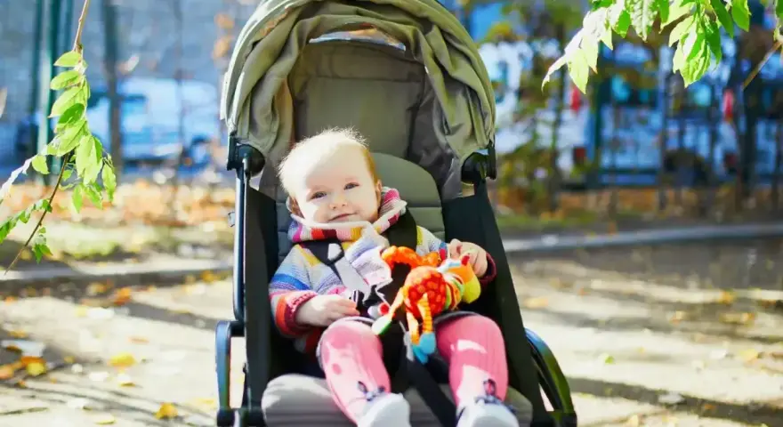 Uśmiechnięte dziecko w wózku spacerowym, z kolorową zabawką. Czas na spacer, do kiedy gondola posłuży?