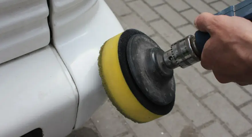 Ręka trzyma polerkę z żółtą gąbką, która poleruje biały zderzak. Dowiedz się, jak wypolerować samochód.