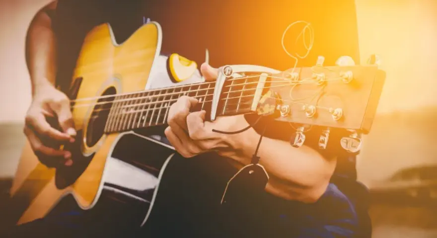 Osoba gra na gitarze akustycznej. Zastanawiasz się, ile trwa nauka gry na gitarze? To zależy od Ciebie!
