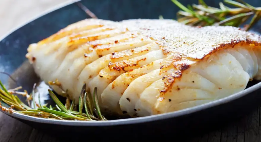 En saftig bit fryst torsk i ugn, gyllene och perfekt tillagad, med rosmarin i en mörk panna.