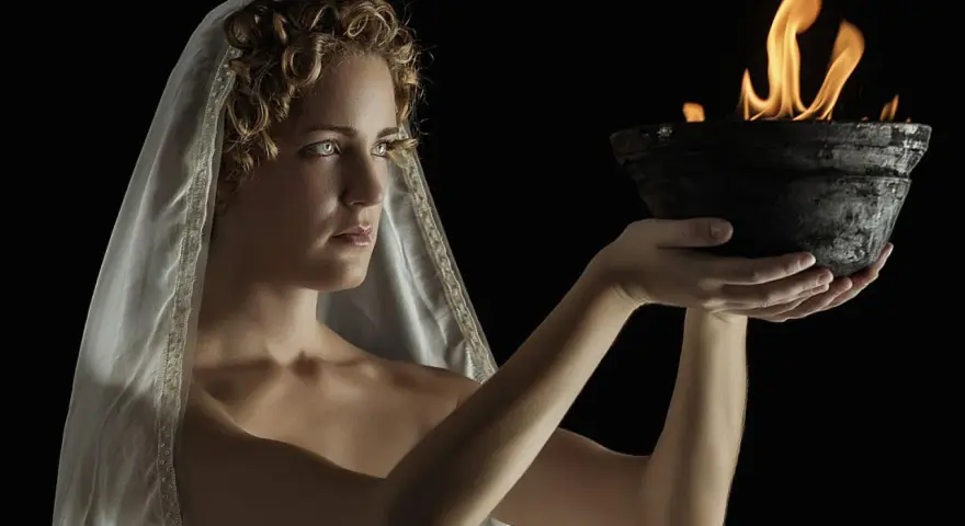 A woman with curly hair and a veil, embodying Hestia goddess, holds a bowl with a sacred flame.