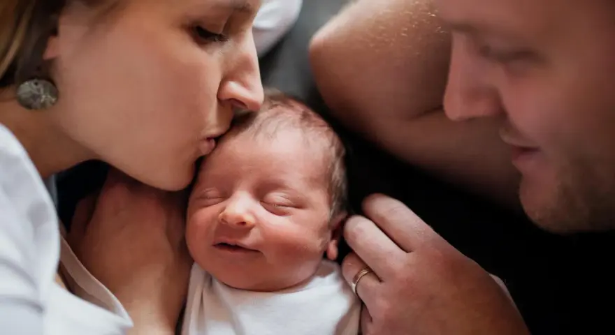 Mutter küsst ihr Neugeborenes, Vater schaut liebevoll zu. Diese Momente sind unbezahlbar, auch nach 1000 Tagen.