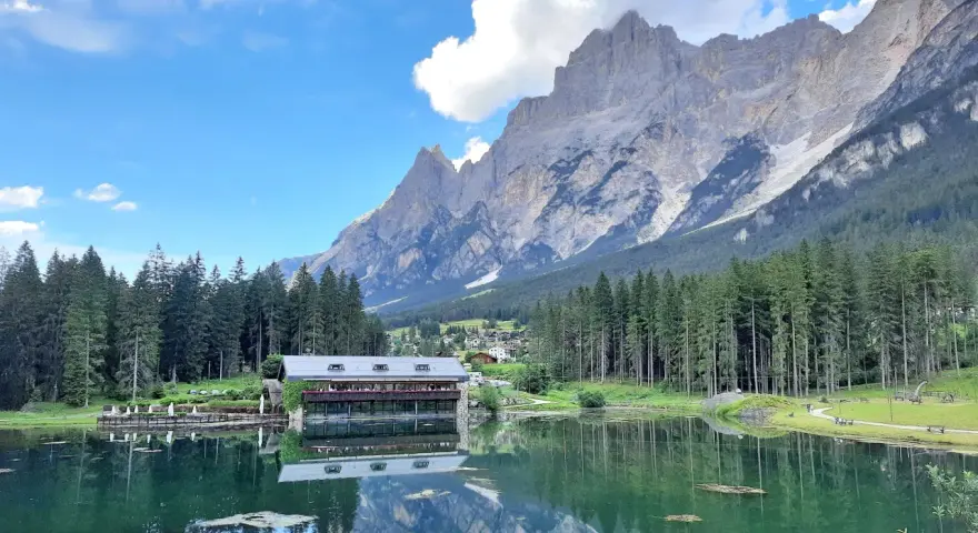 Riflessi alpini sul lago di Mosigo, con un rifugio e montagne imponenti sullo sfondo.