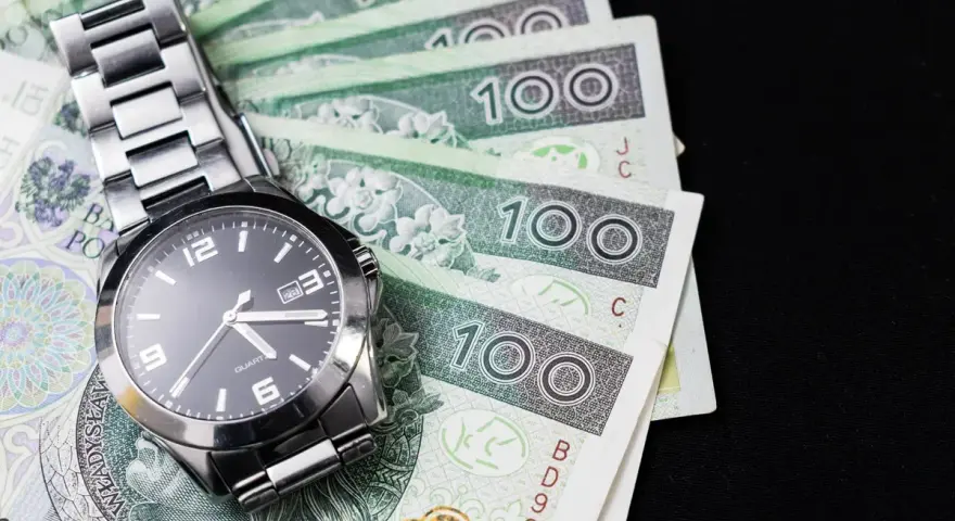 Zegarek na stosie banknotów 100 zł. Czas to pieniądz, a ten schemat zachowań kompulsywnych pokazuje, jak łatwo można stracić kontrolę nad finansami.