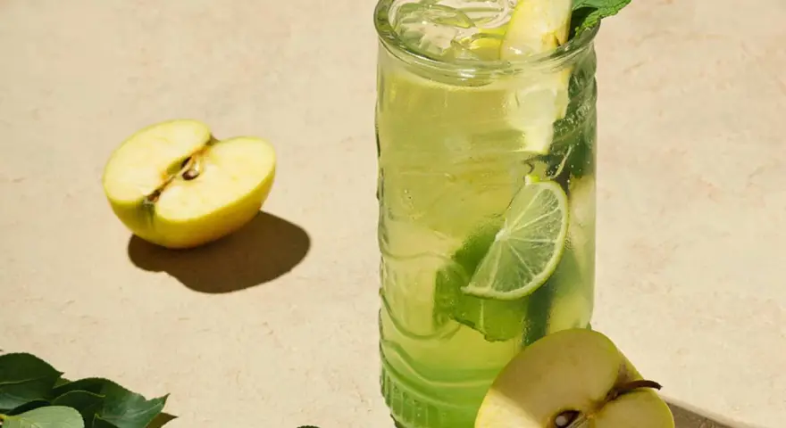En uppfriskande p2 drink med äpple, lime och mynta. Två halvor av ett grönt äpple ligger bredvid glaset.