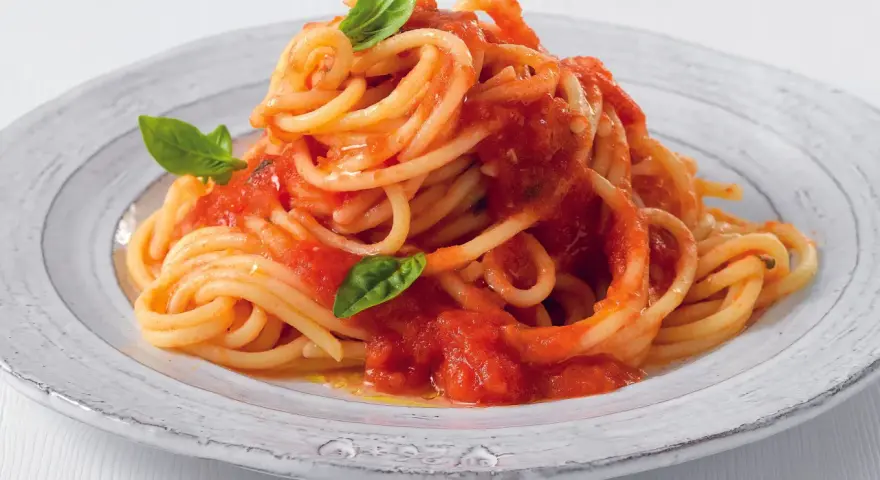 Un piatto di pasta fatta in casa, spaghetti al pomodoro fresco e basilico, serviti su un piatto rustico.