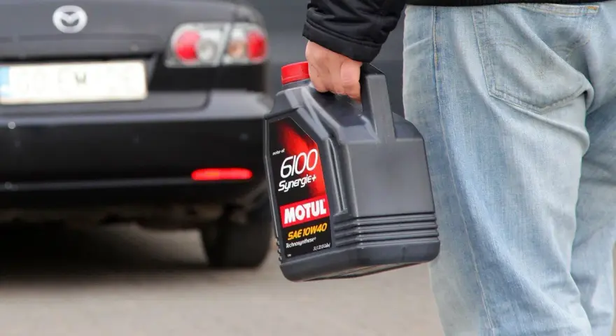 Mężczyzna niesie kanister z olejem silnikowym Motul. W tle czarna Mazda.