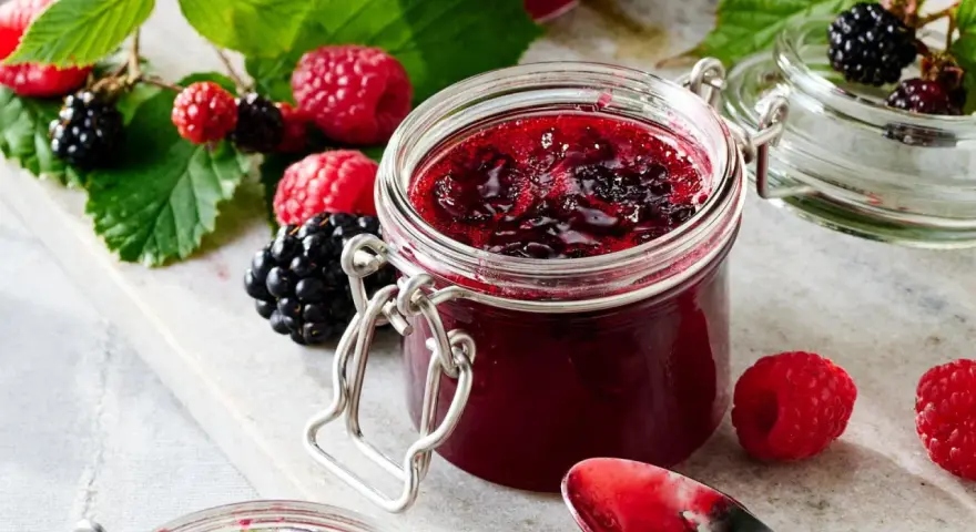 Frische Brombeeren und Himbeeren neben einem Glas selbstgemachter Marmelade. Perfekt für brombeeren rezepte schnell und einfach.