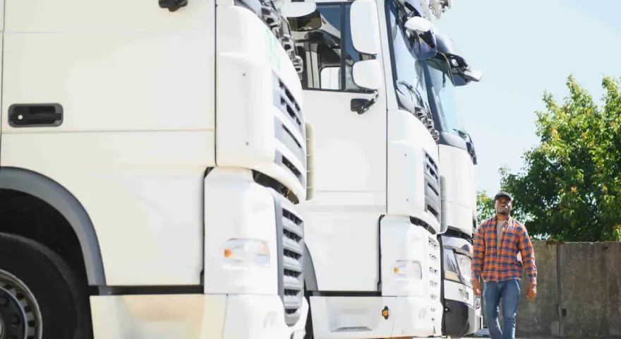 Kierowca idzie obok rzędu białych ciężarówek. To właśnie spedycja co to – transport towarów na dużą skalę.