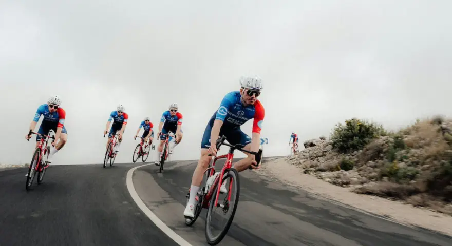 Cyclists in blue and red kits race downhill, showcasing the intense effort behind the Tour de France average speed.