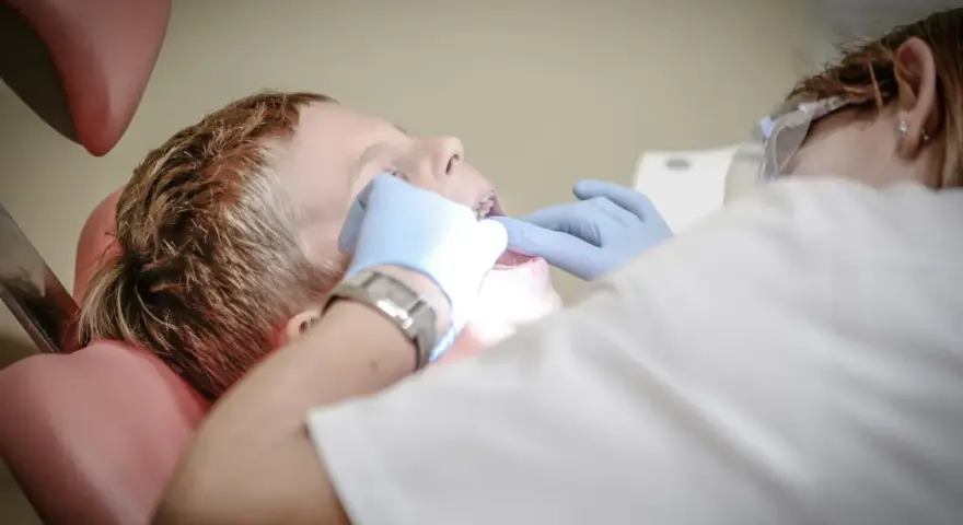 Chłopiec siedzi na fotelu dentystycznym podczas wizyty u dentysty. Dentysta w rękawiczkach bada jego zęby.