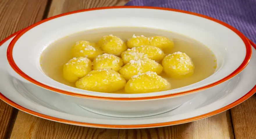 Una ciotola di semolino dosi per 1 persona, con palline dorate in brodo, cosparse di formaggio grattugiato.