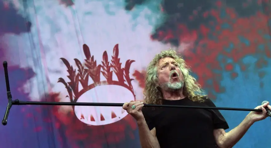 Wokalista Led Zeppelin, Robert Plant, śpiewa z pasją na tle scenografii z koroną.