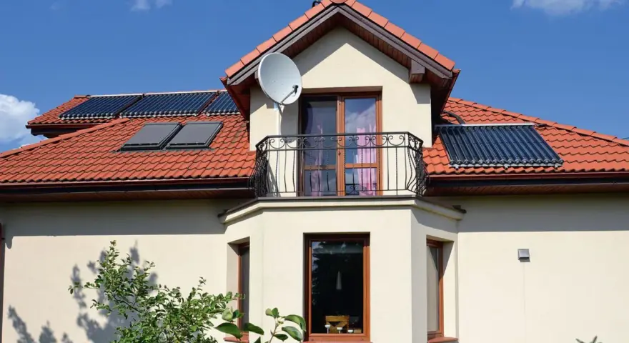 Elegancki wykusz w domu z balkonem i anteną satelitarną. Na dachu widoczne kolektory słoneczne.
