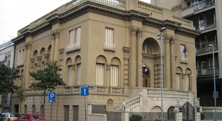 Elegancki budynek, Muzeum Tesli, z kolumnami i łukami. Przed nim schody i ogrodzenie.