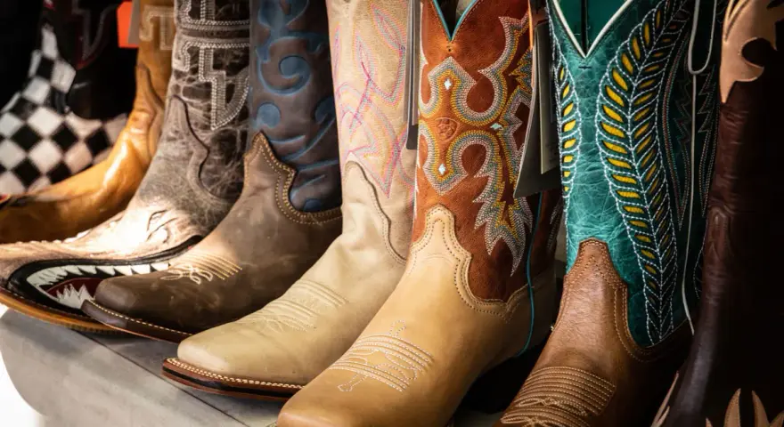 Una fila di stivali da cowboy colorati e ricamati, mostrando la differenza tra texani e camperos con vari design.
